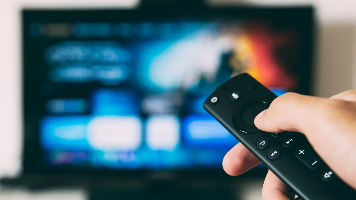 Hand holding a streaming stick remote pointed at a TV showing a home screen